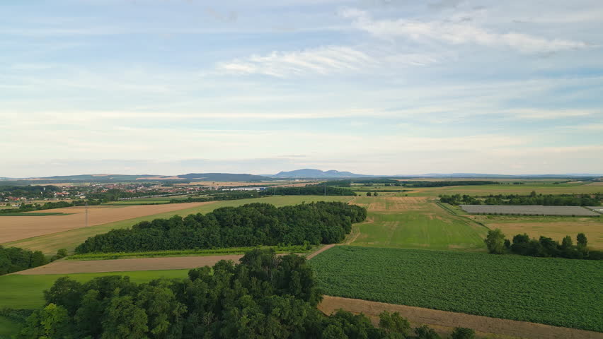 Aerial drone view of fields and small woodlands with the rolling hills of Pálava in the background. The elevated perspective showcases the harmonious blend of agriculture, nature, and the scenic count