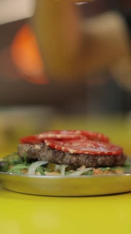 A vertical closeup footage of a chef making a hamburger in a stainless plate on a yellow table, with blurred background