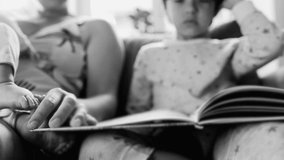 Close-up of mother pointing to a book while sitting with her children on the couch, a quiet and intimate family moment in black and white monochrome - Powered by Shutterstock - Get 15% off with code: PIKWIZARD15