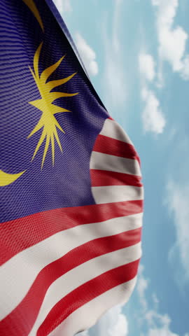 Wavy flag of Malaysia blowing in the wind in slow motion. Waving official Malaysian flag team symbol abstract vertical background. Blue sky with clouds. World countries flying flags concept