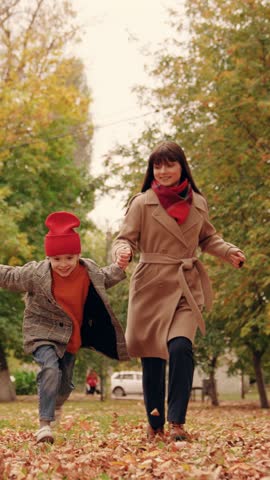 Kid daughter, mom, dad play together holding hands in autumn outdoor. Happy child run holding hands of his mom dad through autumn yellow leaves in park. Active family walk, mother child father in park