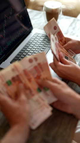 Vertical cropped shot of unrecognizable business team celebrating successful stock market trade with pile of Russian rubles banknotes, reaping big profits from their investment sitting at table.