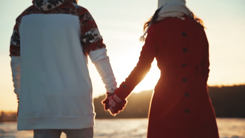 Back view of couple holding hands wearing gloves at winter sunset. Happy couple dating at sunny day outside at Christmas holidays. spend time together at Christmas eve. Girl and a guy relationship
