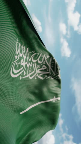 Wavy flag of Saudi Arabia blowing in the wind in slow motion. Waving official Saudi Arabia flag team symbol abstract vertical background. Blue sky with clouds. World countries flying flags concept