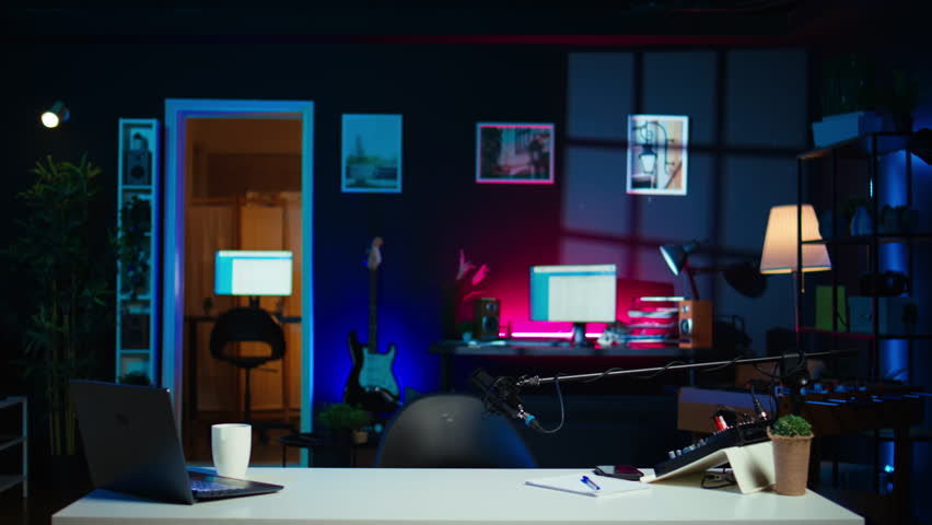 Playful internet star using microphone to shoot video, doing frantic gesturing. Energetic content creator hiding under desk while filming vlog with professional mic in home studio, camera B