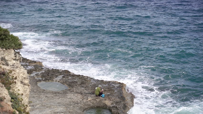 A fisherman is during fishing. A man is fishing with a beautiful view of the rocks and the sea.