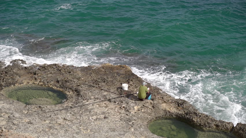 A man is fishing with a beautiful view of the rocks and the sea.