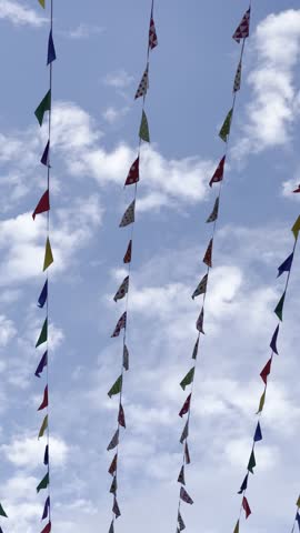 Shot of coloured birthday celebration pennants waving in the in blue sky. Colorful triangle bunting flags or banderitas hanging and blown by wind against blue sky. Celebration and fiesta concepts.