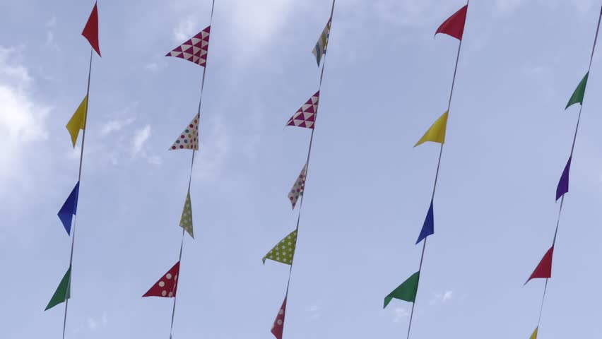 Shot of coloured birthday celebration pennants waving in the in blue sky. Colorful triangle bunting flags or banderitas hanging and blown by wind against blue sky. Celebration and fiesta concepts.