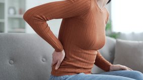 Close up. Female hand holding massaging lower back. Tired young adult woman suffering from back pain while sitting on sofa in living room at home. Upset lady shows discomfort due to poor posture - Powered by Shutterstock - Get 15% off with code: PIKWIZARD15