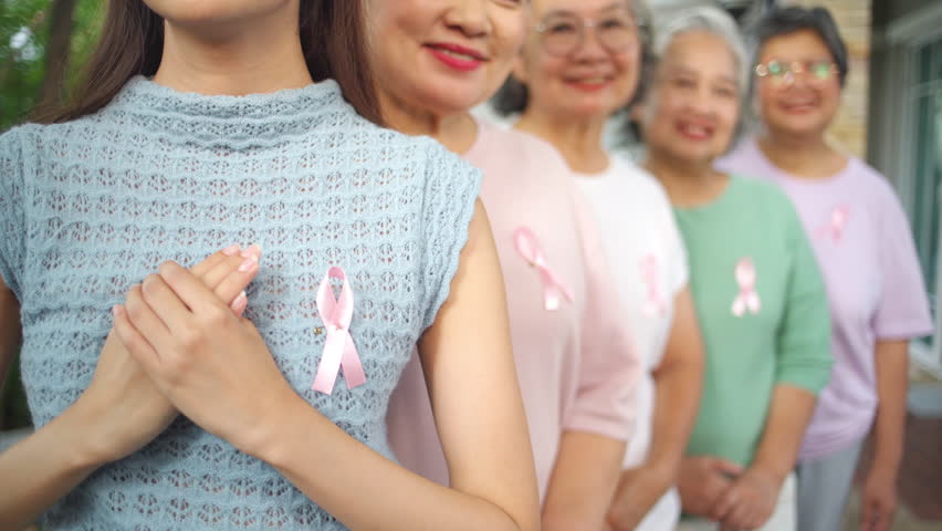 Breast Cancer Awareness Charity Concept. Portrait Group of Smiling Asian senior mature and adult women wearing T-Shirts with breast cancer symbol pink ribbon on the left side.