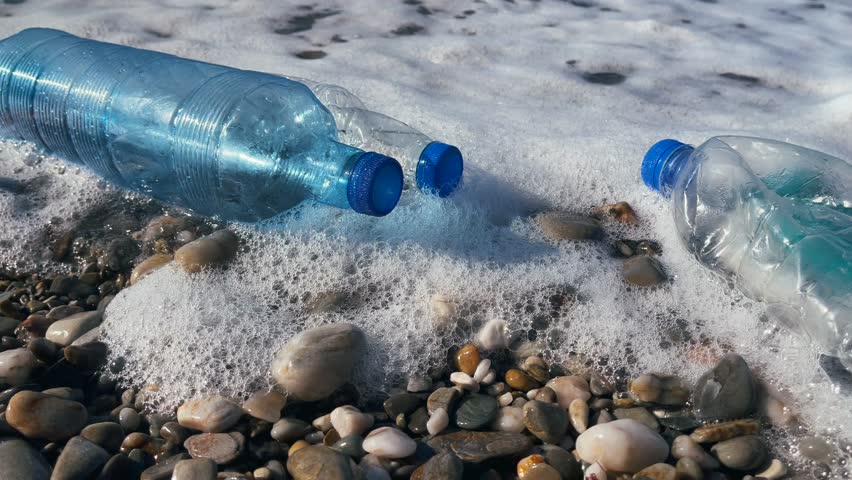 Close-up of plastic bottles in the surf, surrounded by foam and rocks