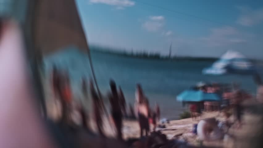 Extreme close up of sunglasses reflecting a sunny beach with people, lake and trees. Summer vacation concept.