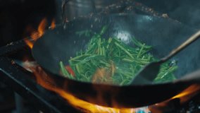 Asian chef tossing and throwing mix of green vegetables with red chilli peppers on wok pan on open fire stove. Vegetarian meal getting cooked by stir frying method with steam spreading over. - Powered by Shutterstock - Get 15% off with code: PIKWIZARD15