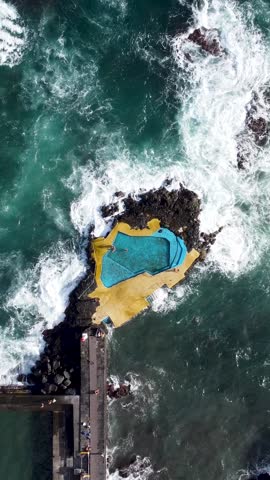 An aerial vertical footage of Caloura natural swimming pool (Piscina de Caloura) on Agua de Pau Beach in Sao Miguel island, Azores, Portugal