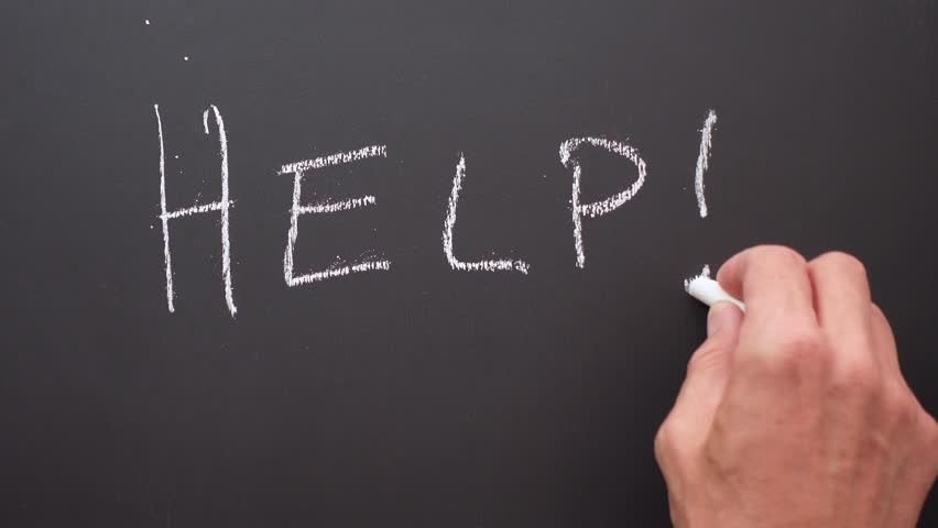 A hand writes the word help with white chalk on a black board