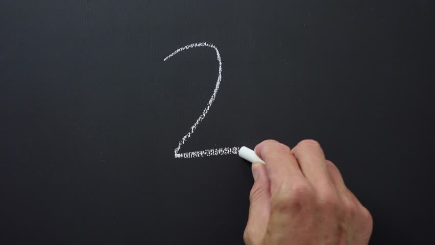 Hand writes the number 2 with white chalk on a black board