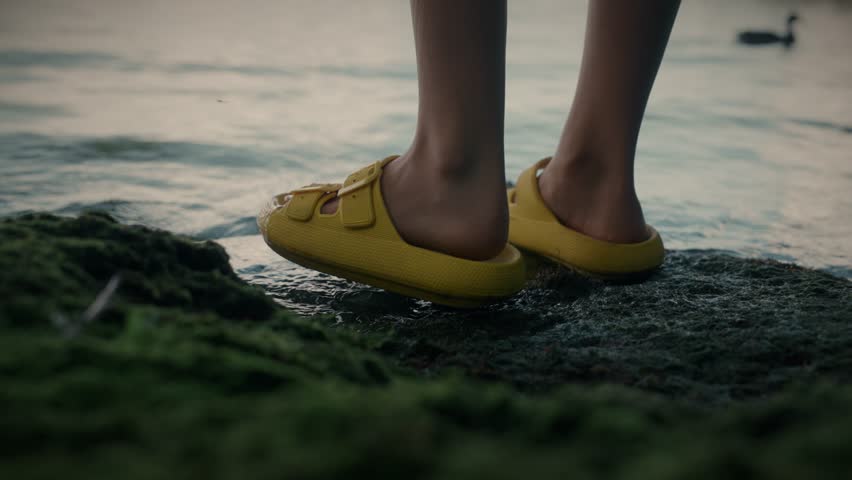 Feet in flip-flops stand on the lake shore