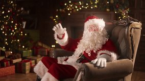 Santa Claus telling fairytales, congratulations and greeting, portrait in home. Old man in Santa costume talking to camera, sitting alone in armchair in cozy decorated room in Xmas eve, slow motion - Powered by Shutterstock - Get 15% off with code: PIKWIZARD15