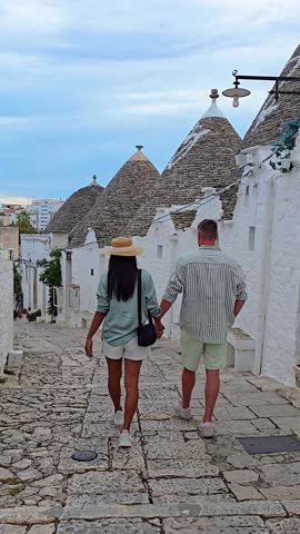 A romantic stroll through the iconic trulli houses of Alberobello captures the essence and charm of Puglia, Italy, as a couple enjoys their lovely day together amidst this unique landscape