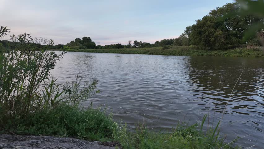 A time-lapse footage of the Grand River flowing through green fields at sunset in Waterloo city, Ontario, Canada