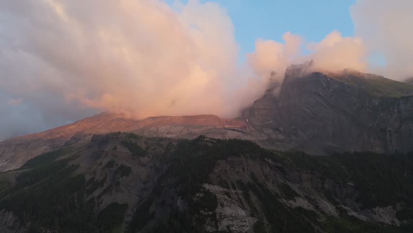 An aerial footage of the clouds touching the Alps peaks around the Oeschinen Lake (Oeschinensee) at sunset in Kandersteg, Switzerland