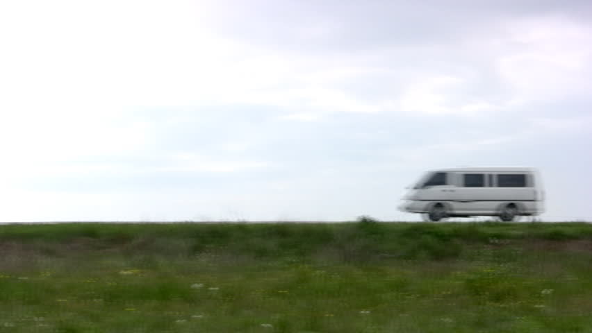 White van quickly goes on the steppe highway against the backdrop of cloudy