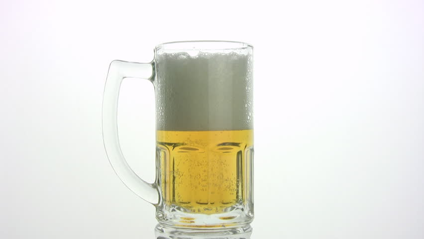 The beer by a jet is poured in mug. beer foam is poured through edge of mug, and