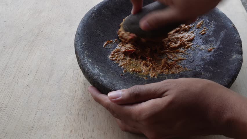 Stir up the chili sauce using a mortar, The hand that is mashing the chili sauce using a mortar, the process of grinding chili sauce using a mortar.