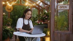 Asian female florist using digital computer while working at green shop with open sign on door. Careful small business owner taking customer orders online at personal website with products selling. - Powered by Shutterstock - Get 15% off with code: PIKWIZARD15