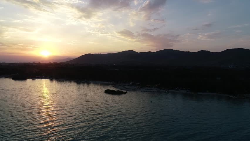 A drone view of a calm lake at sunset with silhouetted mountain
