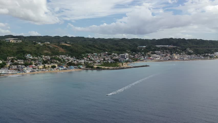 A high drone footage of speedboat sailing near to Rompeolas Beach (Playa Rompe Olas) and Bandera de Puerto Rico view in Aguadilla, Puerto Rico
