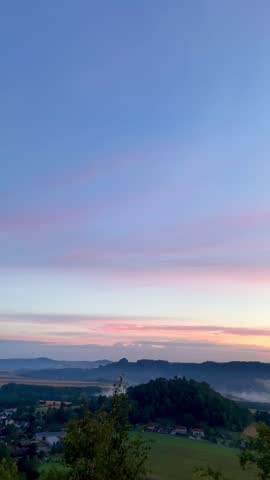 A beautiful landscape in the dawn with a sunrise over a hill and clouds hanging in the valley filmed from the top of the Mountain after a hike.