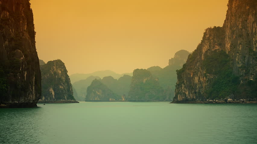 A landscape scene of the Ha Long Bay rocky cliffs with orange sunset sky in Vietnam