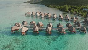 Luxurious overwater bungalows huts with thatched roofs standing in rows on turquoise lagoon water of Moorea island in French Polynesia. Exotic travel vacation getaway, romantic honeymoon. Aerial shot - Powered by Shutterstock - Get 15% off with code: PIKWIZARD15