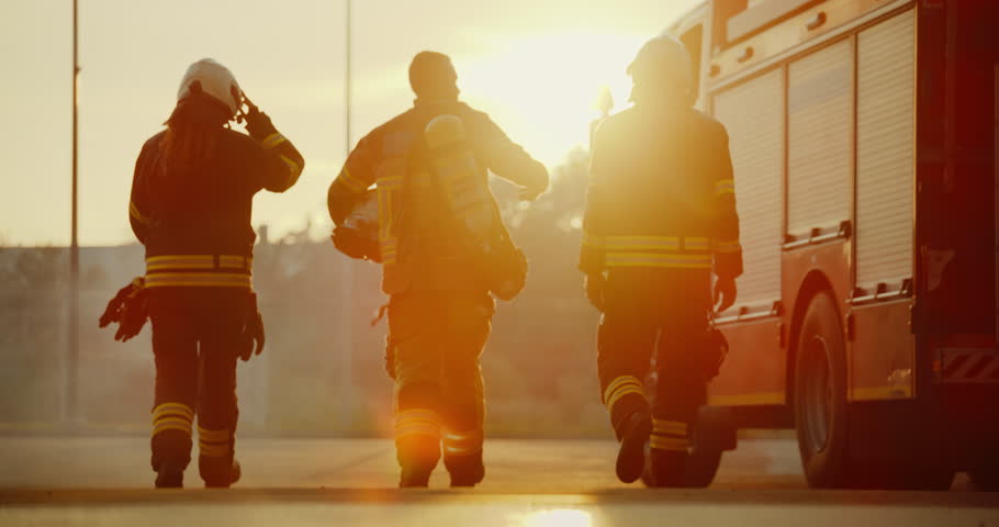 Diverse Team of Firefighters in Full Gear Walking Towards a Fire Truck at Sunset, Ready for Action. Scene Captures Their Unity, Bravery and Dedication to Saving Lives in Emergencies