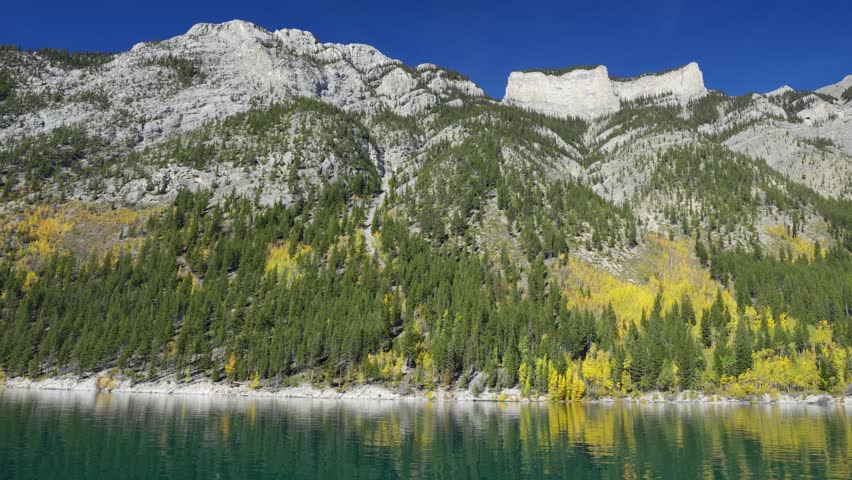 Lake Minnewanka Cruise in autumn. Banff National Park, Alberta, Canada. Canadian Rockies majestic mountains, forests in yellow green color against blue sky.