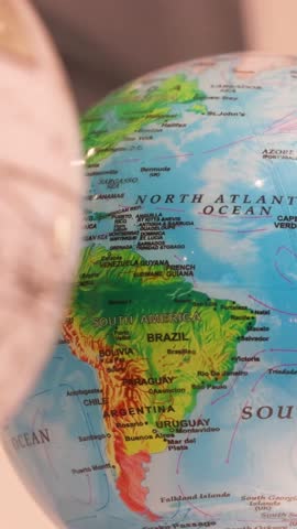 On a small globe, South America appears as a landmass in the southern and western hemispheres, showcasing countries like Brazil and Argentina, with notable features like the Andes mountains 