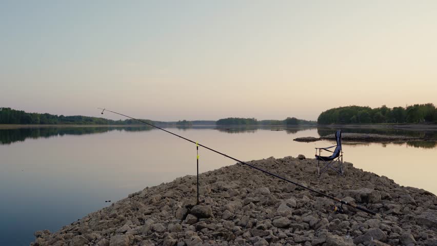 Fishing setup on a rock by the river in a summer evening without a fisherman. Fishing rod and fishing chair by the river.