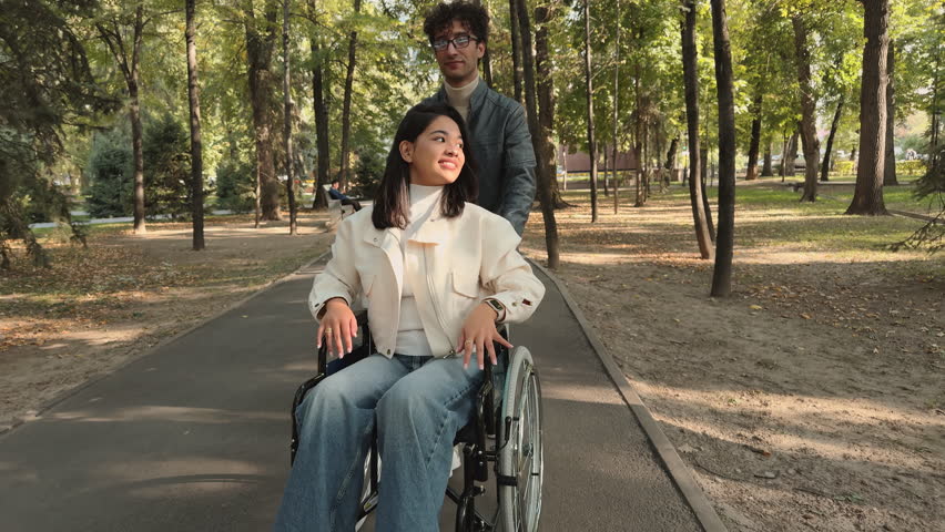Boyfriend pushing girlfriend in wheelchair smiling and raising arms