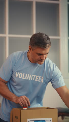 Middle-aged male volunteer packing donated goods into boxes at charity center