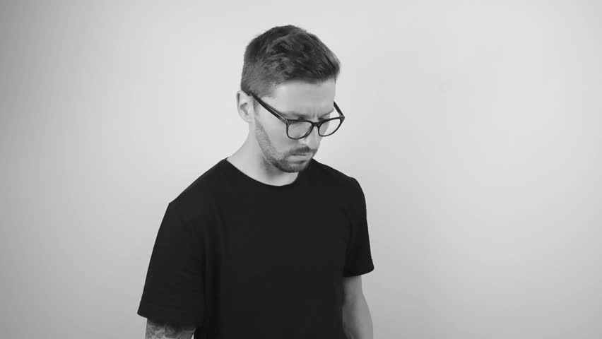 Footage of a tattooed man with a full sleeve and wristband wearing glasses and searching something from a book. Then points it out and looks at the camera. Footage is on white background in slowmotion