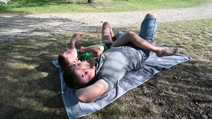 Dad and son rest in the shade under a tree, summer vacation in nature.