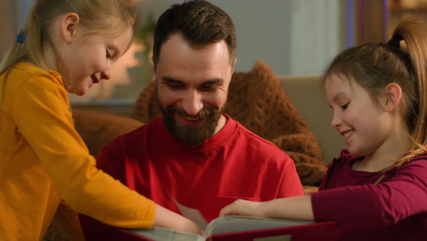 Caucasian family happy father dad adult man and children kids siblings daughters little girls schoolgirls holding book photo album pictures smiling parental custody at home evening weekend together