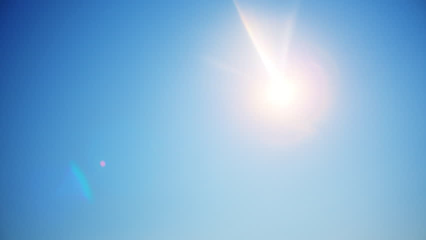 Bright sun shines in the clean blue sky. Sun flare in bright summer sky.