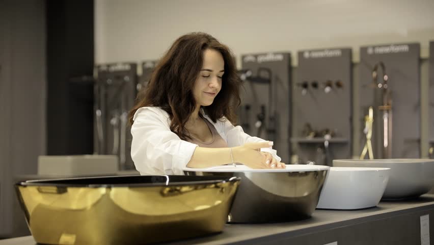 Beautiful young attractive woman chooses modern bathroom sinks. 