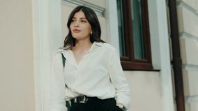 Portrait of a young woman in a white shirt and black pants posing confidently by a building outdoors. Young Woman in Casual Outfit Posing Outdoors by Building - Powered by Shutterstock - Get 15% off with code: PIKWIZARD15