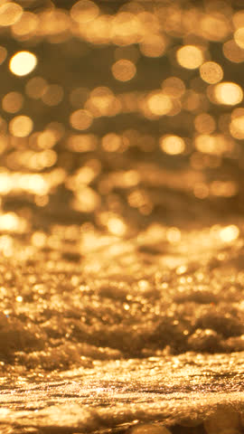 Golden sunset on the beach. Foamy waves rolling towards golden sand beach under low warm sun light. Slow motion. Nobody. Holiday recreation concept. Abstract nautical summer ocean sunset nature.