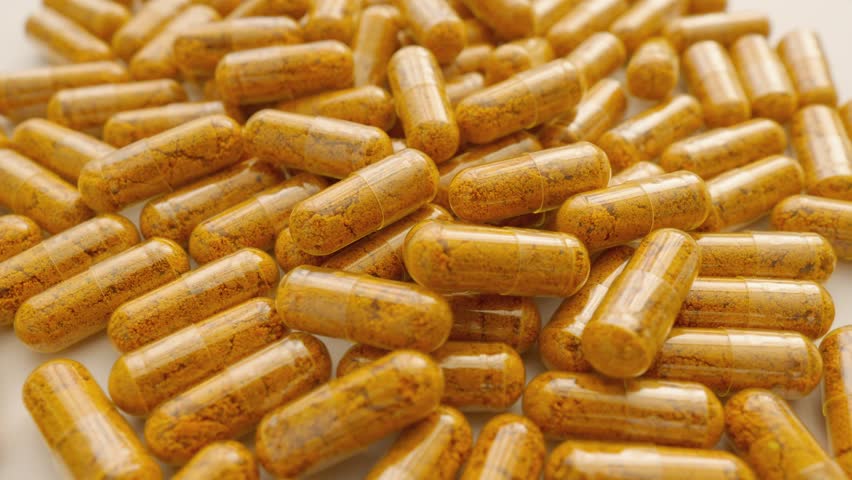 Orange capsules of turmeric dietary supplement with pepper. Capsule collection on white background, spinning to rhythm health. Path to Healthy Life: Pharmaceutical Industry in Production of Capsules.