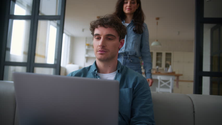 Caucasian woman girl female wife girlfriend come in living room home hug embrace neck hugging male man husband boyfriend guy freelancer laptop addict working online couple together talking shopping